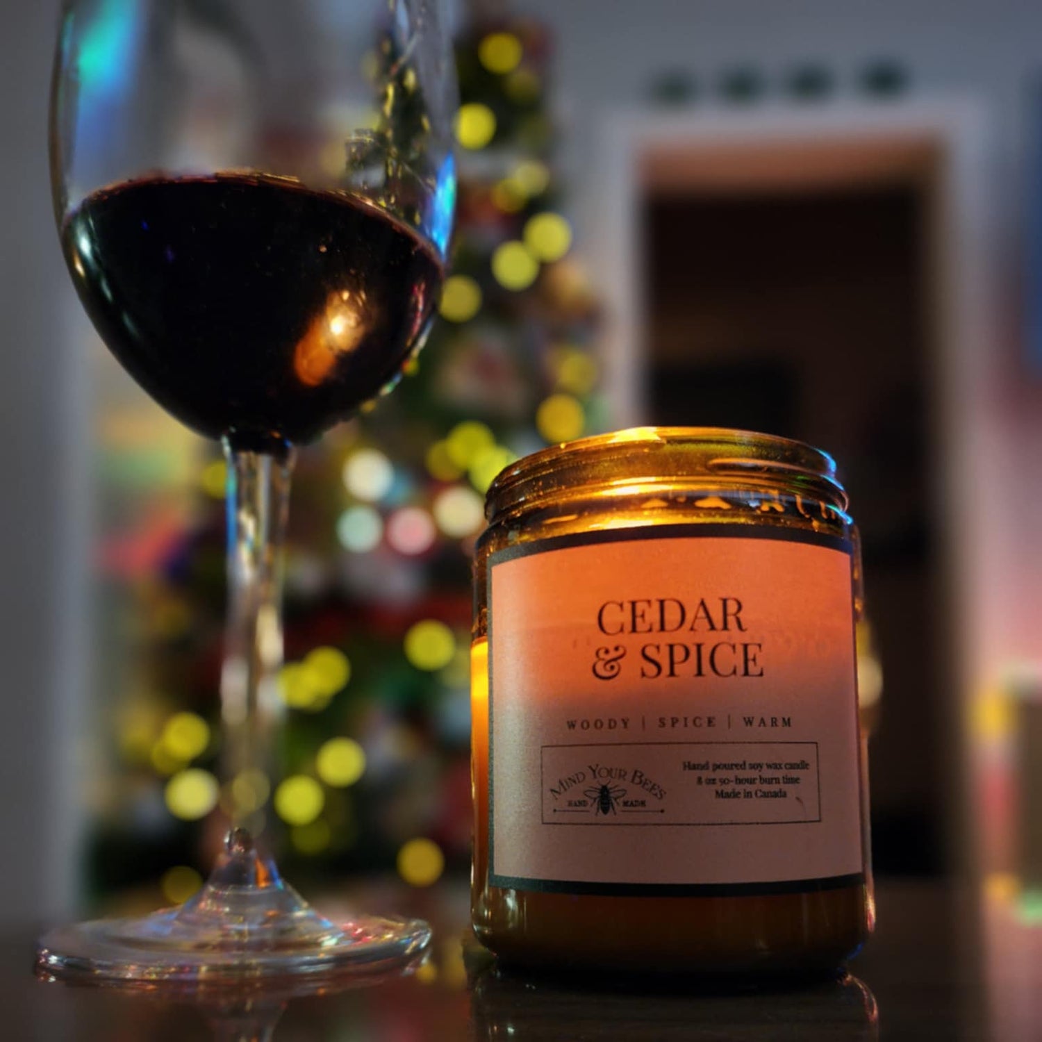Candle labeled 'Cedar & Spice' next to a glass of red wine with a blurred festive background