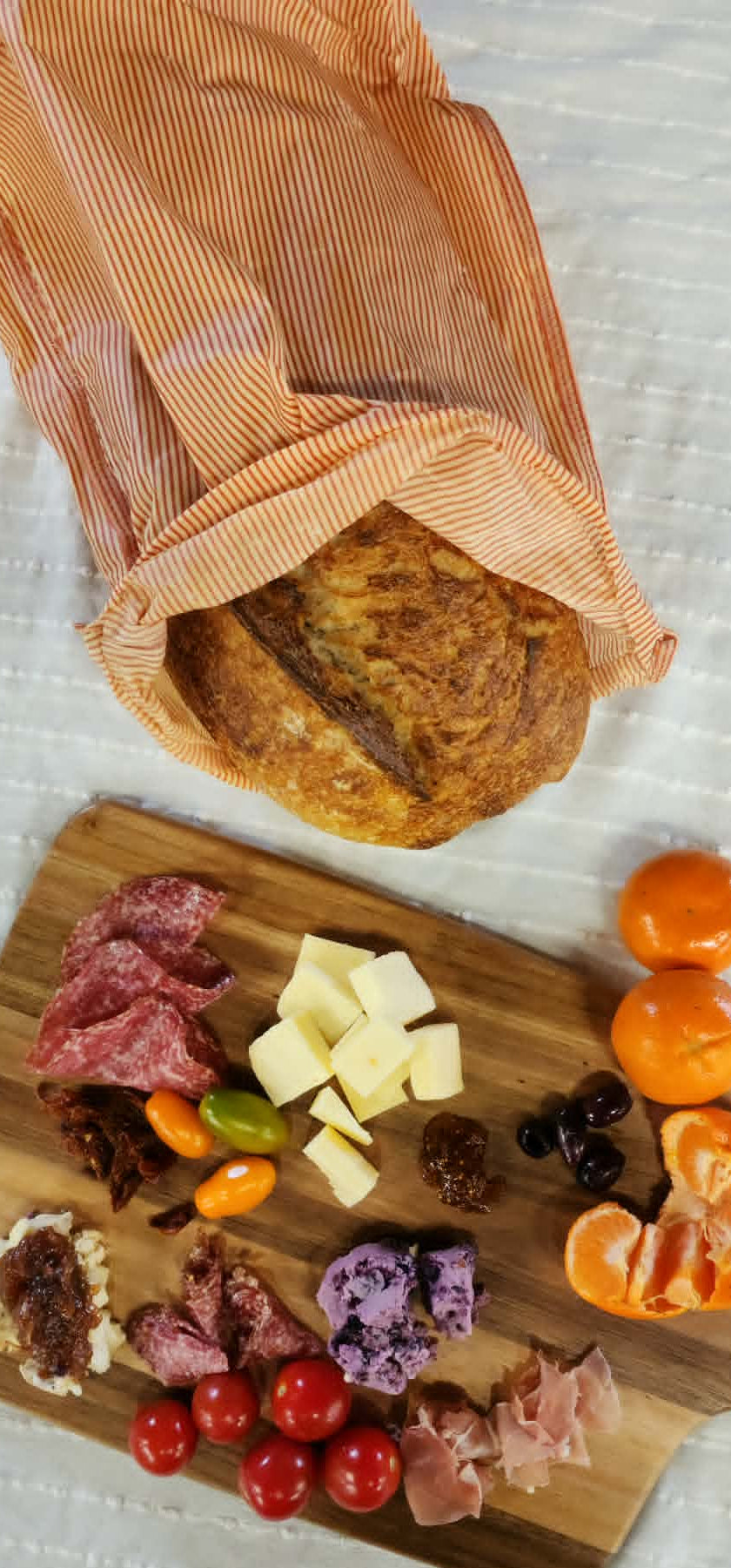 Wooden cutting board with assorted meats, cheeses, and fruits on a white surface